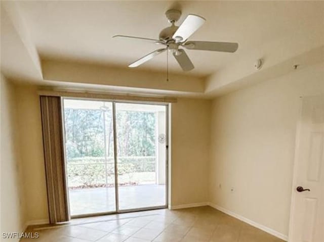 spare room featuring baseboards, a ceiling fan, a raised ceiling, and light tile patterned floors