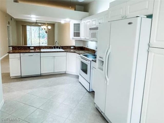 kitchen with dark countertops, a notable chandelier, a sink, white appliances, and white cabinetry