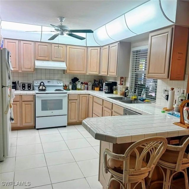 kitchen featuring freestanding refrigerator, a peninsula, white range with electric cooktop, under cabinet range hood, and a sink