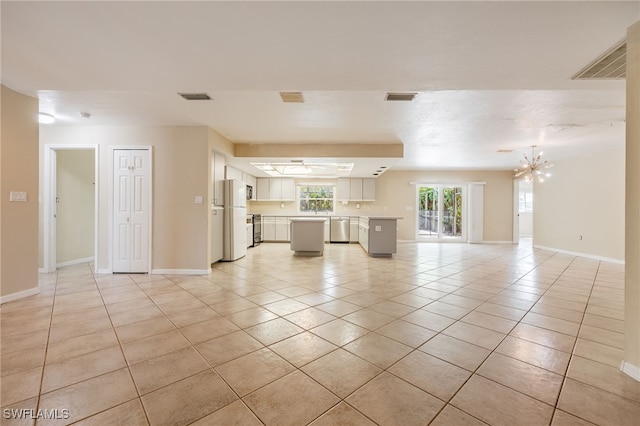 unfurnished living room featuring baseboards, a chandelier, light tile patterned flooring, and visible vents