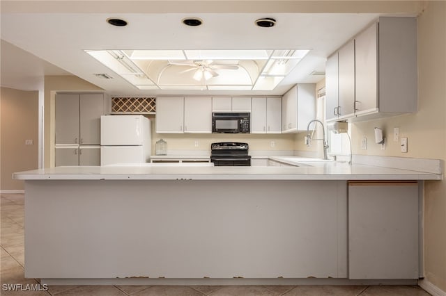kitchen featuring freestanding refrigerator, a peninsula, black microwave, stainless steel electric range, and a sink