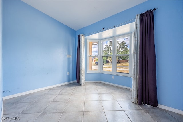 spare room with light tile patterned floors, baseboards, and lofted ceiling