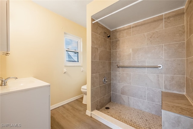 bathroom featuring vanity, wood finished floors, toilet, and tiled shower