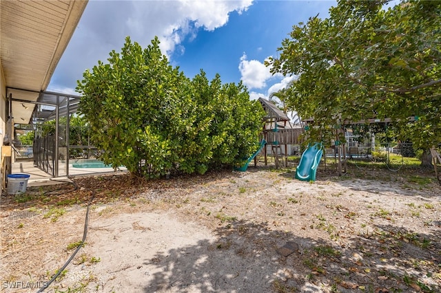 view of yard featuring glass enclosure, fence, a fenced in pool, and a playground