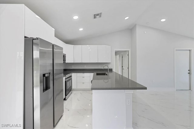 kitchen featuring marble finish floor, dark countertops, a sink, appliances with stainless steel finishes, and vaulted ceiling