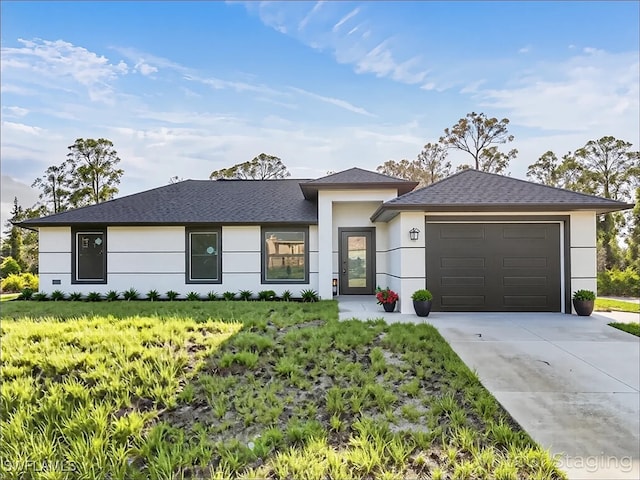 prairie-style home with a garage, a front yard, roof with shingles, stucco siding, and concrete driveway