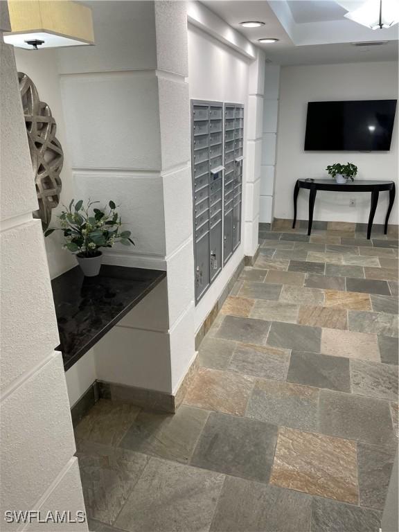 hall featuring mail area, stone tile floors, and baseboards