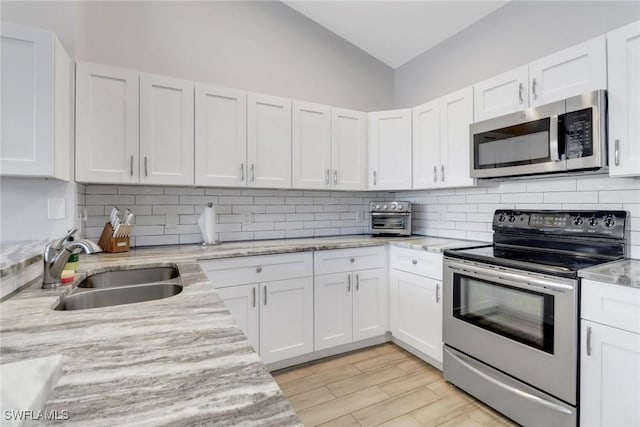 14831 Blackbird Ln, Fort Myers, FL 33919 - kitchen featuring appliances with stainless steel finishes, a sink, tasteful backsplash, white cabinets, and vaulted ceiling