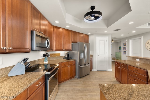 3414 Hancock Bridge Pkwy Unit 502, North Fort Myers, FL 33903 - kitchen with appliances with stainless steel finishes, ceiling fan, a tray ceiling, light wood finished floors, and brown cabinetry