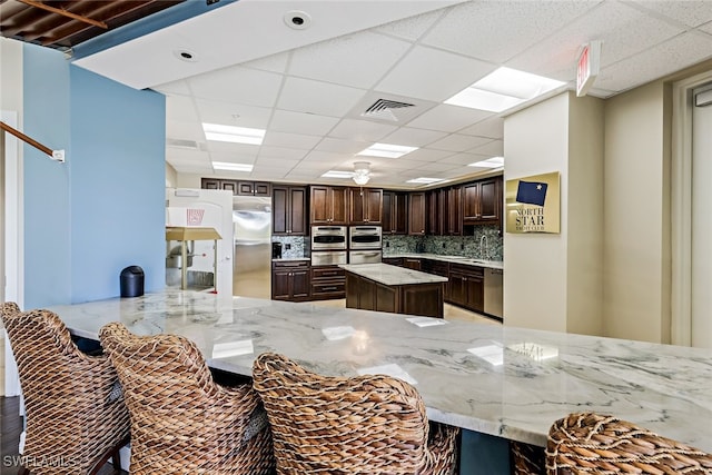 3414 Hancock Bridge Pkwy Unit 502, North Fort Myers, FL 33903 - kitchen with appliances with stainless steel finishes, a drop ceiling, light stone countertops, dark brown cabinetry, and tasteful backsplash