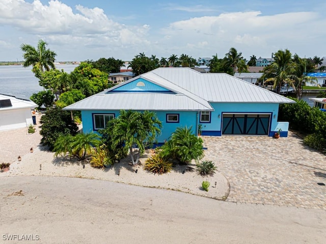 view of front of house featuring metal roof, decorative driveway, a water view, an attached garage, and stucco siding