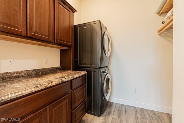 clothes washing area with light wood-style floors, baseboards, stacked washer and dryer, and cabinet space