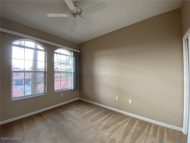 spare room featuring light colored carpet, baseboards, and ceiling fan