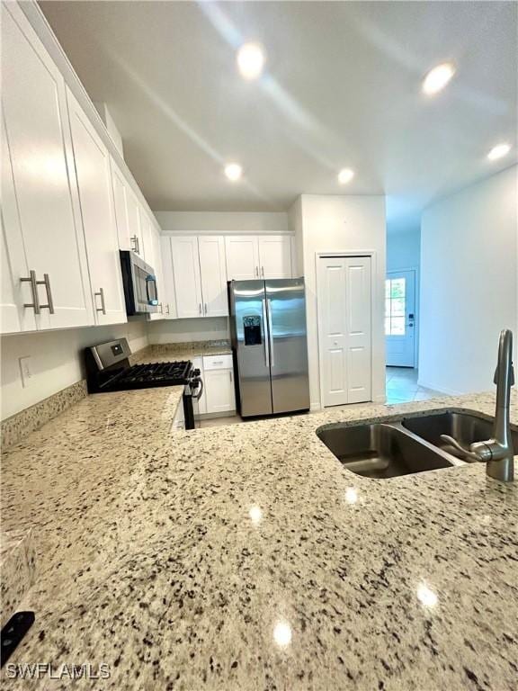 kitchen featuring white cabinets, light stone countertops, a sink, stainless steel appliances, and recessed lighting