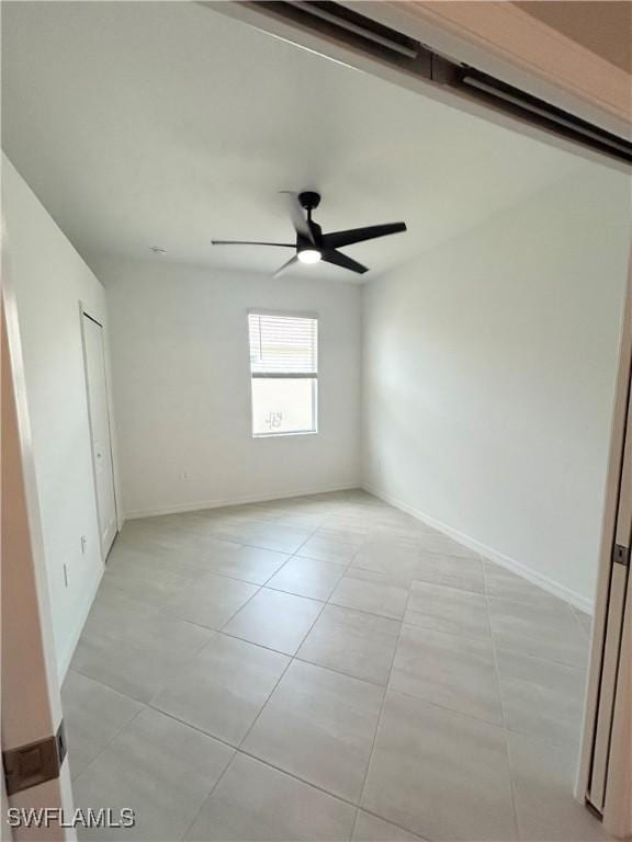 spare room featuring light tile patterned floors, baseboards, and ceiling fan