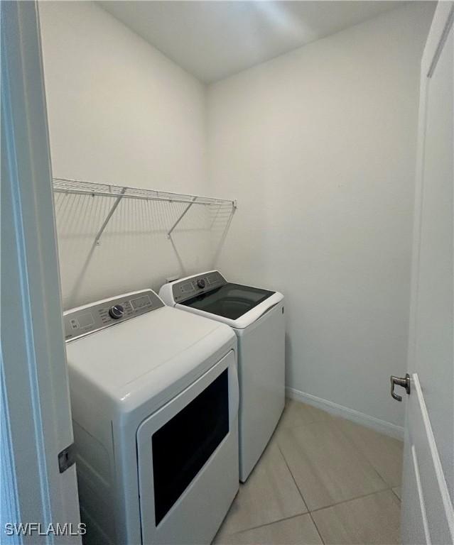 clothes washing area with laundry area, baseboards, light tile patterned flooring, and washer and dryer