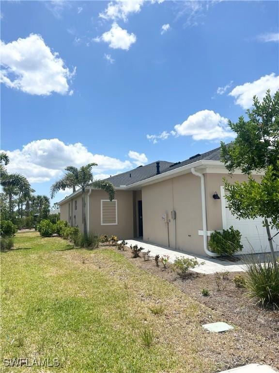 view of side of property featuring a lawn, an attached garage, and stucco siding