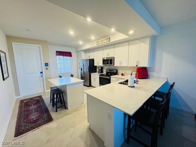 5629 Double Eagle Cir Unit 4224, Ave Maria, FL 34142 - kitchen with a breakfast bar, light countertops, white cabinets, a sink, and appliances with stainless steel finishes