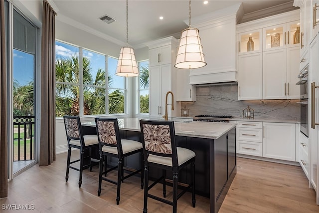 kitchen featuring visible vents, a sink, a kitchen island with sink, and ornamental molding