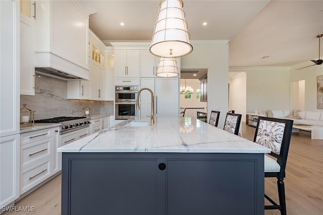 kitchen featuring light stone countertops, appliances with stainless steel finishes, light wood-style flooring, decorative backsplash, and a center island with sink