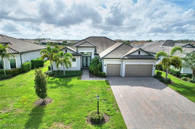 view of front of house featuring a garage, a front yard, decorative driveway, stucco siding, and french doors