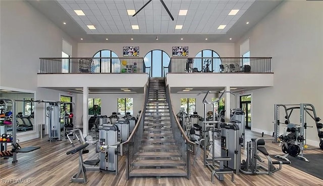 gym with a paneled ceiling, a towering ceiling, and wood finished floors