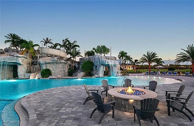 pool at dusk featuring a community pool, a water slide, a fire pit, and a patio area