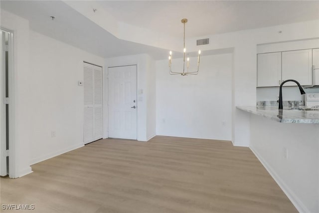 unfurnished dining area featuring a sink, a chandelier, light wood finished floors, and baseboards