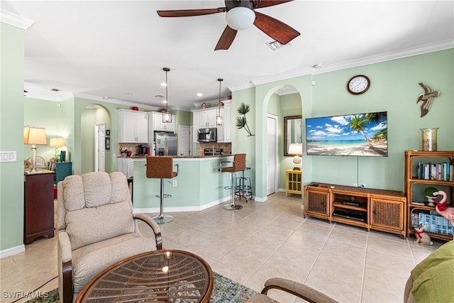 living area featuring crown molding, arched walkways, a ceiling fan, light tile patterned floors, and baseboards
