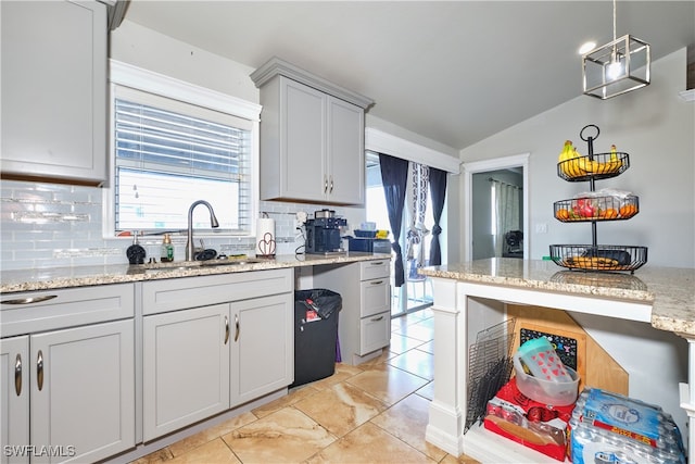 kitchen with a sink, vaulted ceiling, tasteful backsplash, light stone countertops, and light tile patterned flooring