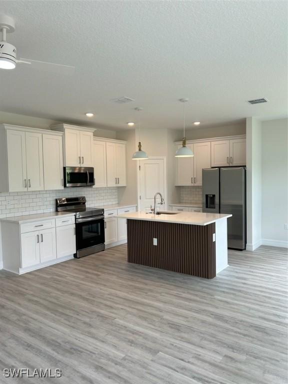 5525 Berryman St, Lehigh Acres, FL 33971 - kitchen featuring appliances with stainless steel finishes, a sink, light wood-style floors, white cabinetry, and tasteful backsplash