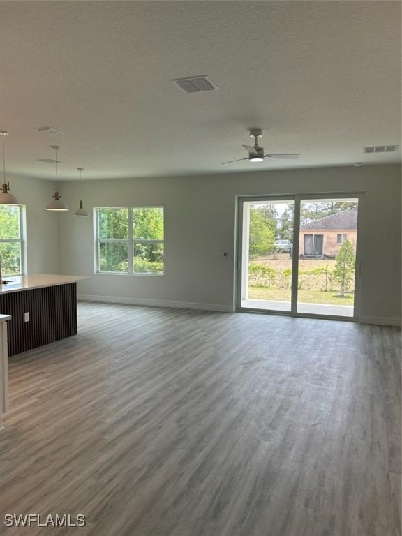 5525 Berryman St, Lehigh Acres, FL 33971 - unfurnished living room featuring a healthy amount of sunlight, baseboards, wood finished floors, and visible vents