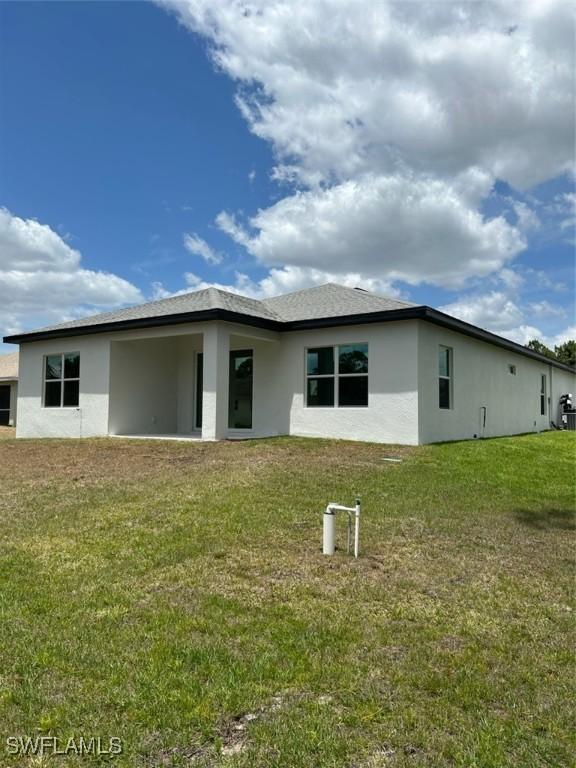5525 Berryman St, Lehigh Acres, FL 33971 - rear view of property featuring a lawn and stucco siding