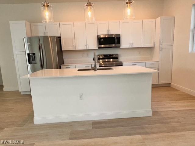 kitchen with a sink, decorative light fixtures, a center island with sink, light countertops, and appliances with stainless steel finishes