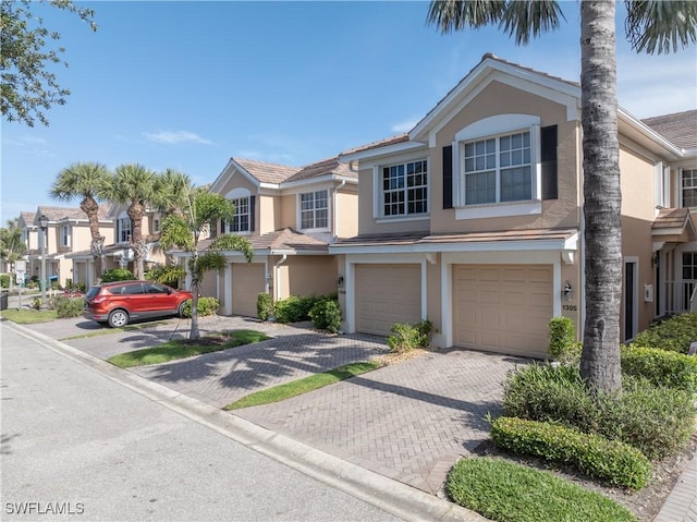 view of property with an attached garage, stucco siding, driveway, and a residential view