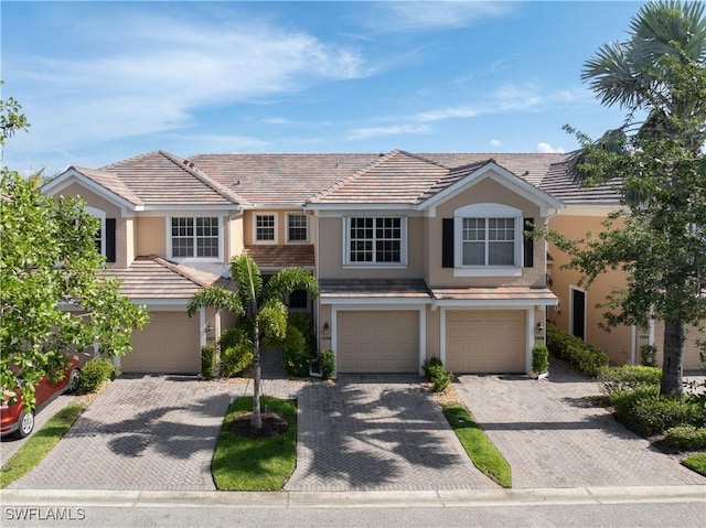 multi unit property with a garage, stucco siding, driveway, and a tile roof