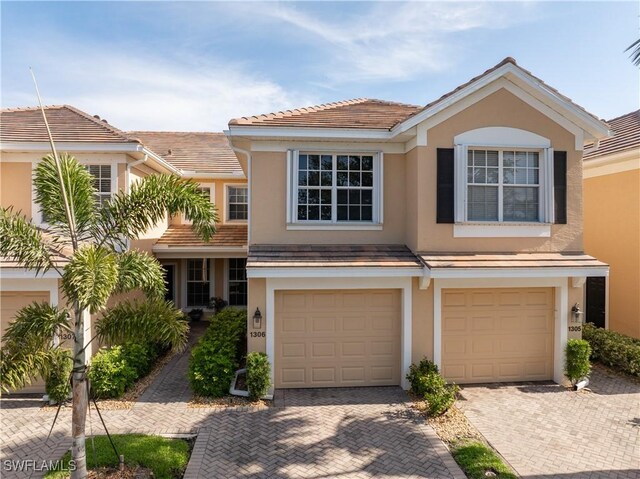 multi unit property with an attached garage, driveway, a tile roof, and stucco siding