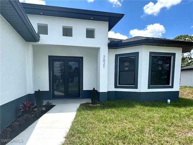 view of exterior entry with a yard, french doors, and stucco siding