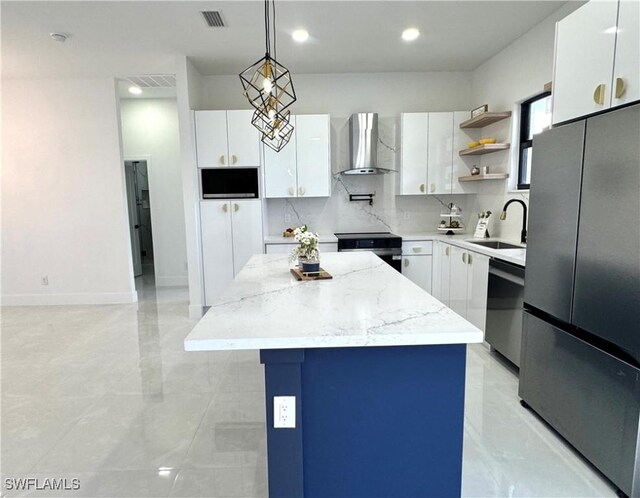 kitchen with visible vents, a kitchen island, wall chimney exhaust hood, a sink, and stainless steel appliances
