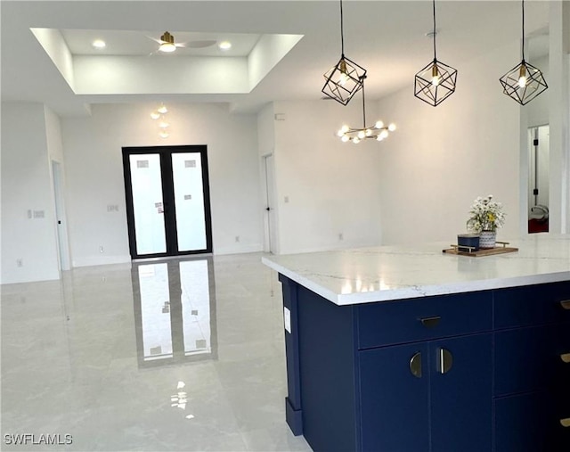 kitchen featuring blue cabinetry, pendant lighting, ceiling fan with notable chandelier, open floor plan, and a tray ceiling
