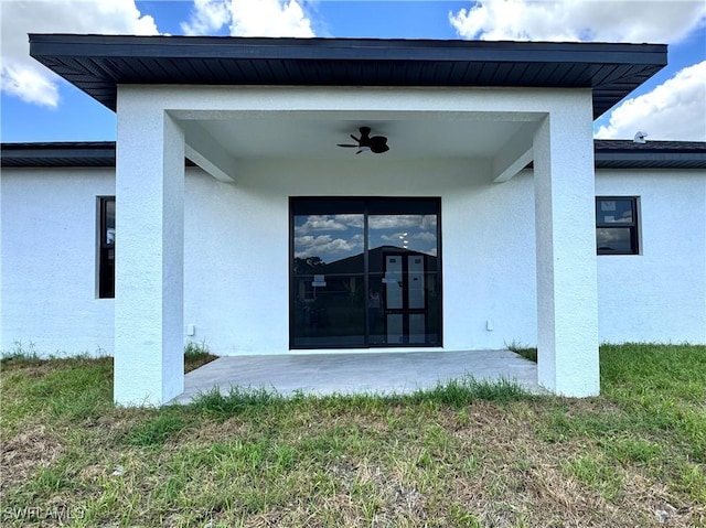rear view of property featuring a ceiling fan, a patio, stucco siding, and a yard