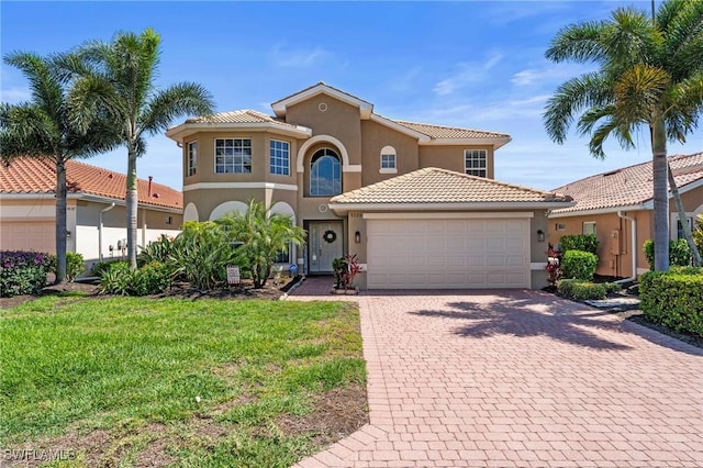 mediterranean / spanish-style house featuring an attached garage, stucco siding, a front lawn, and driveway