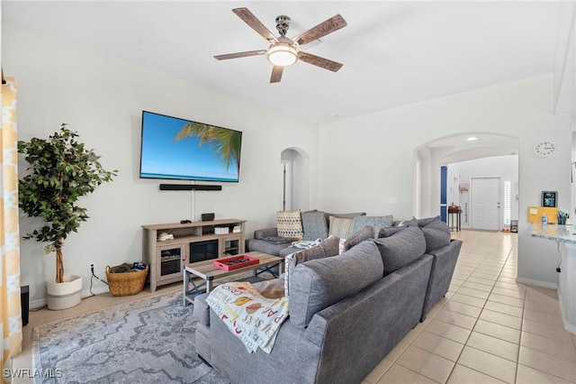 living room with light tile patterned floors, baseboards, a ceiling fan, and arched walkways