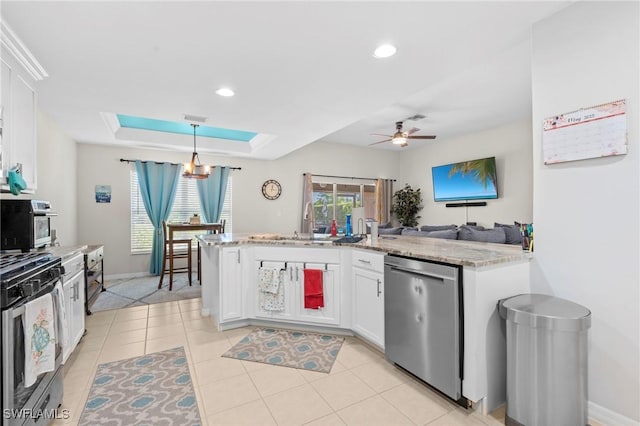 kitchen featuring stainless steel appliances, ceiling fan with notable chandelier, pendant lighting, white cabinetry, and a tray ceiling