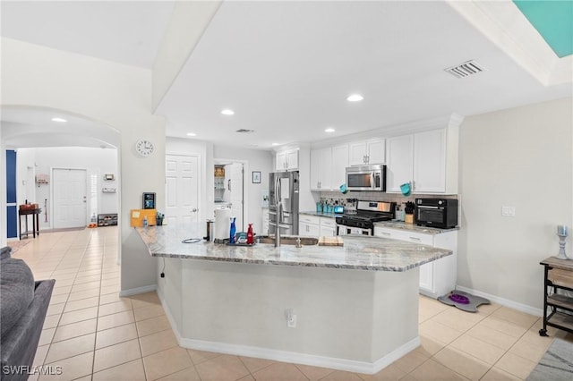 kitchen featuring appliances with stainless steel finishes, light tile patterned floors, arched walkways, and white cabinetry