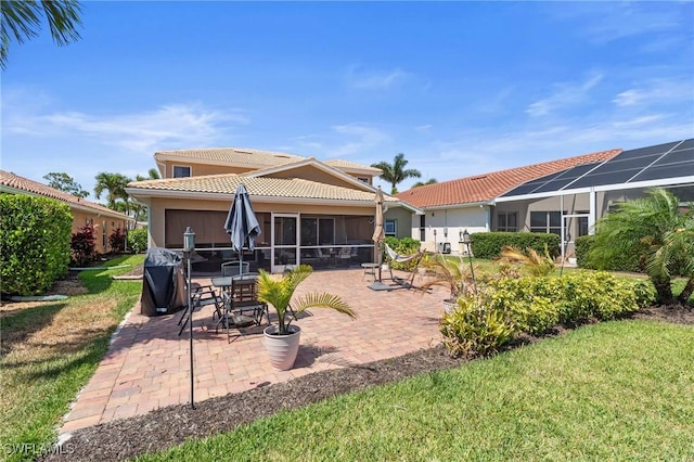 back of house featuring a yard, a patio area, a sunroom, and a tiled roof