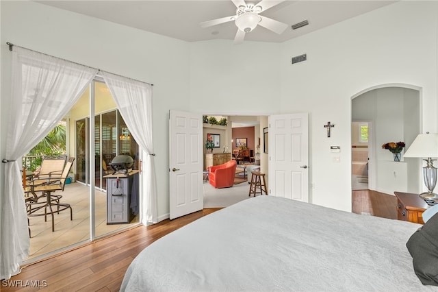 bedroom with arched walkways, access to outside, wood finished floors, and visible vents