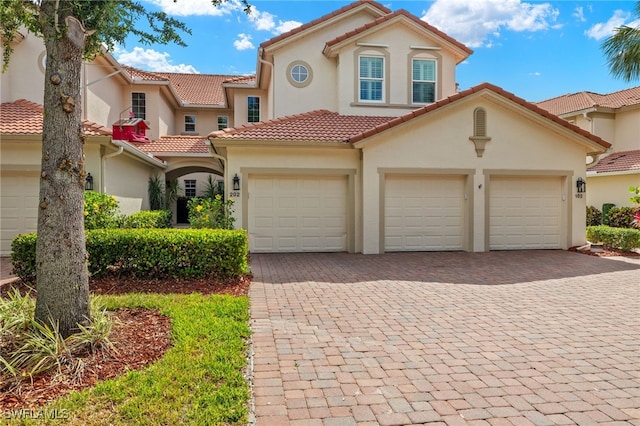 mediterranean / spanish house featuring a tiled roof, stucco siding, an attached garage, and decorative driveway