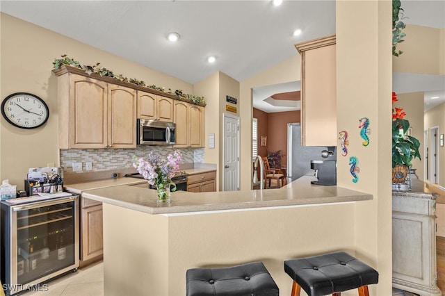 kitchen with decorative backsplash, a kitchen breakfast bar, light brown cabinetry, appliances with stainless steel finishes, and beverage cooler