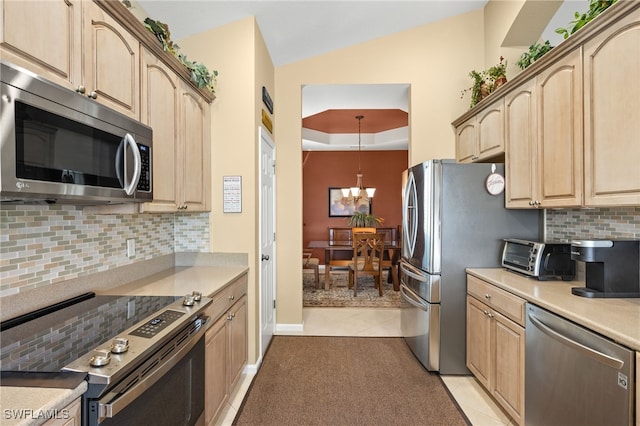 kitchen with appliances with stainless steel finishes, light brown cabinetry, a chandelier, and tasteful backsplash